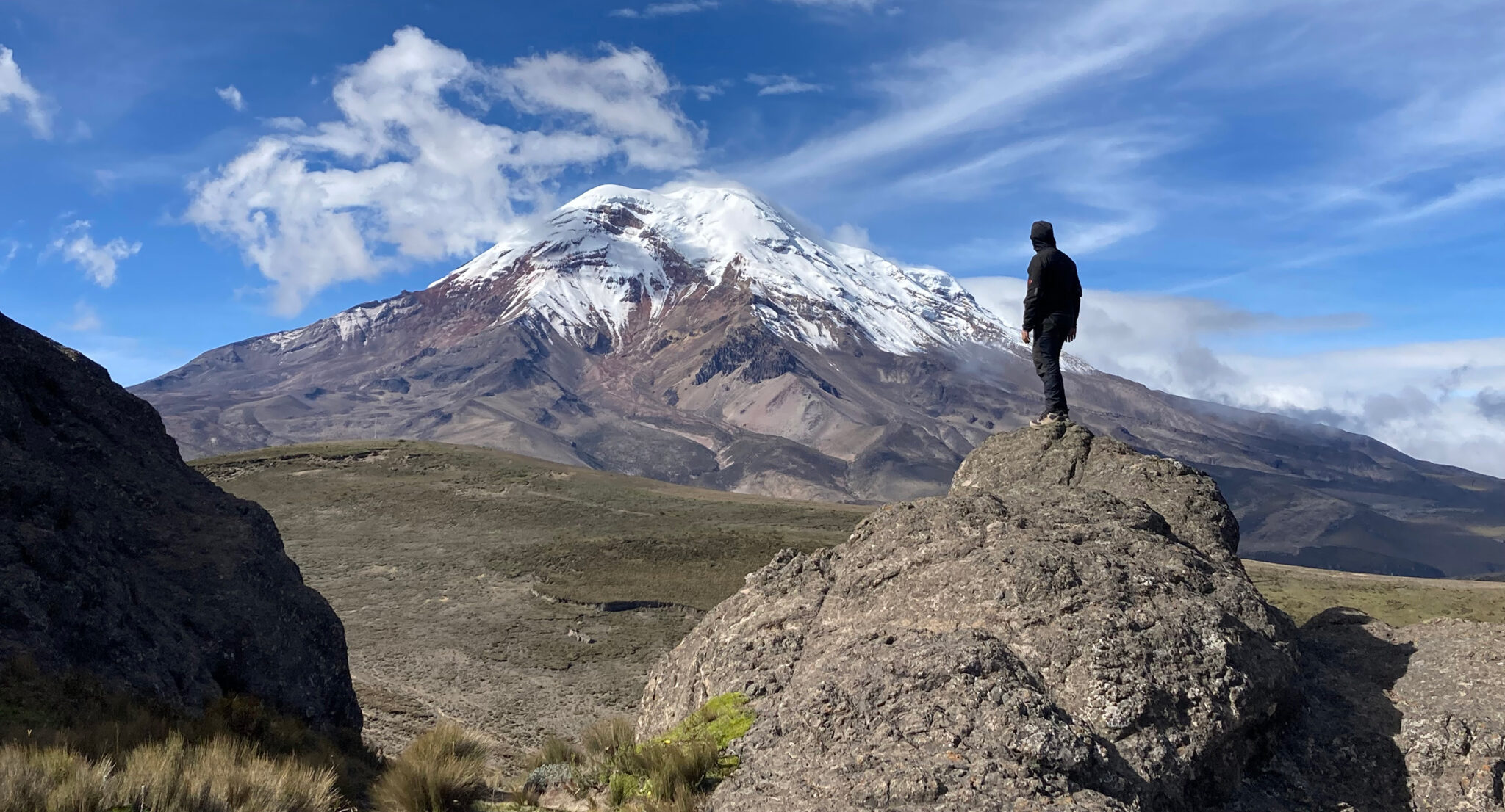 photo of man standing on rock looking at mountain, day