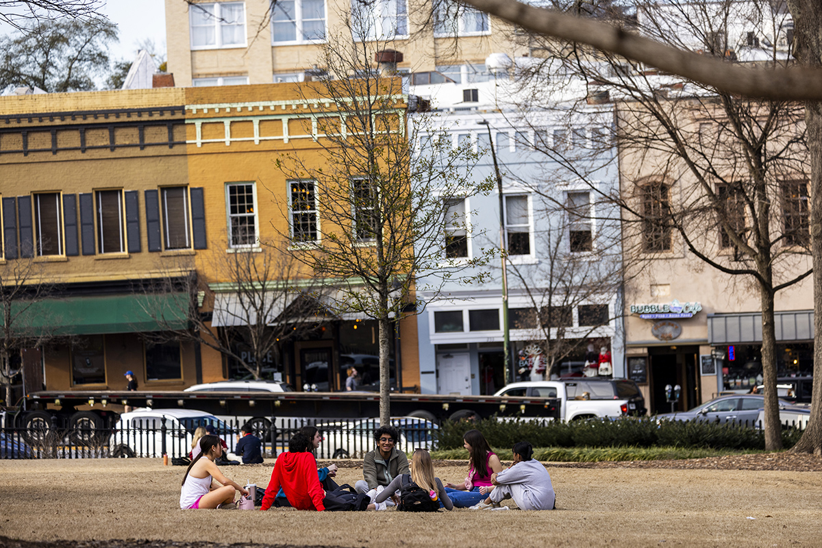 photo of people sitting in grass, day, downtown in background