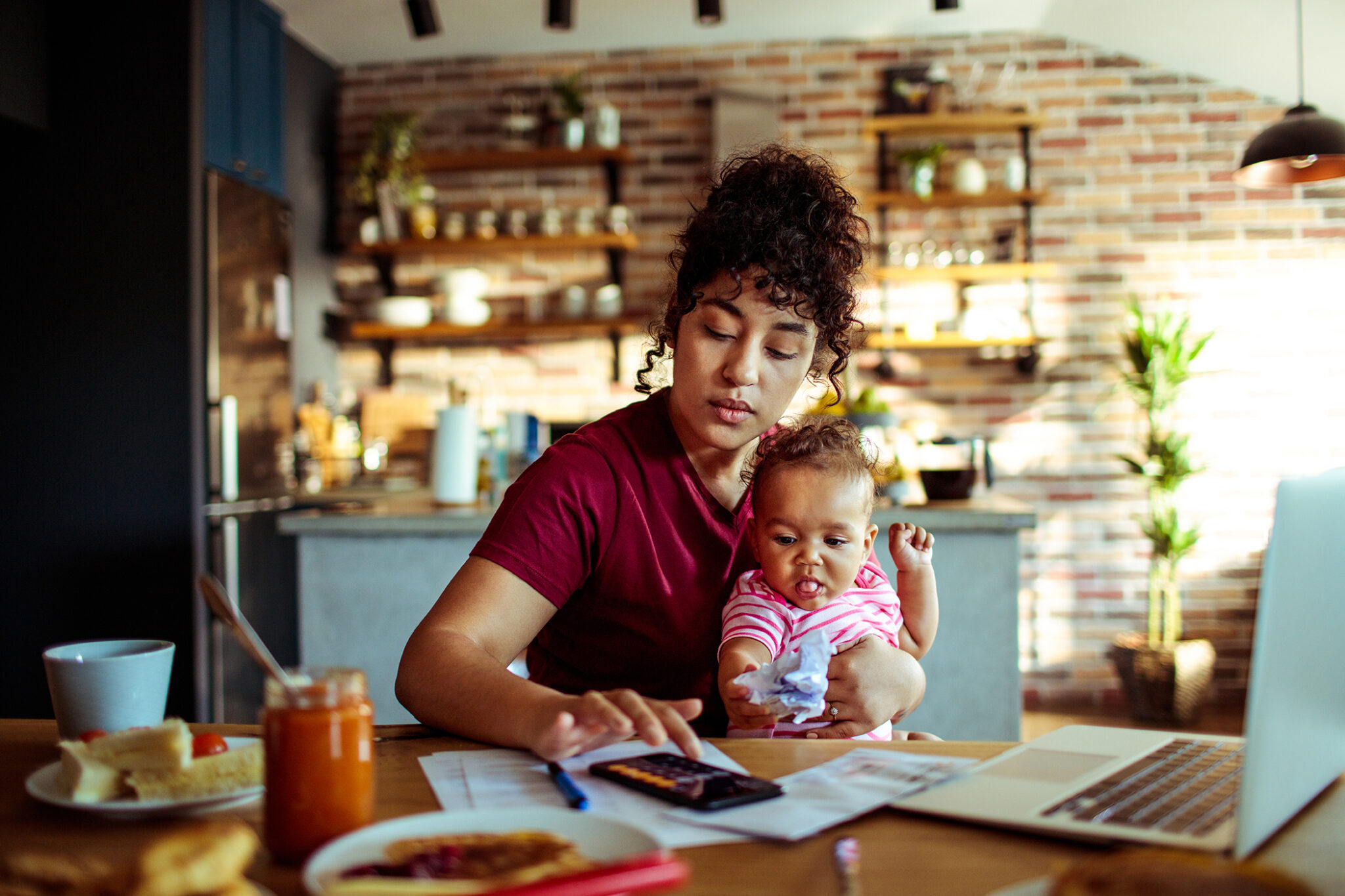 photo of woman holding baby, with laptop in kitchen