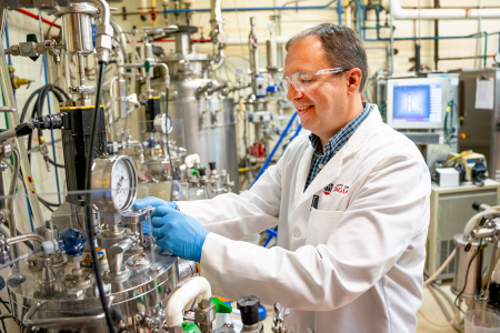 photo of man in lab with tubes, gauges, equipment, monitor